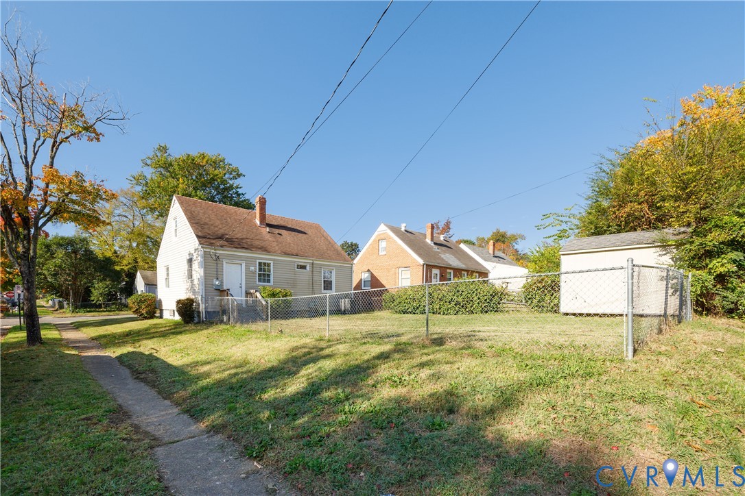 Exterior view featuring a light-colored siding finish, a gable roofline with brick chimneys, and a chain-link fenced yard with a detached storage structure