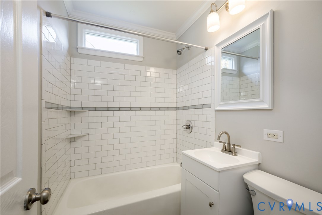 Bathroom featuring white subway tile shower surround with integrated shelving, white pedestal vanity, chrome-finish hardware, and crown molding