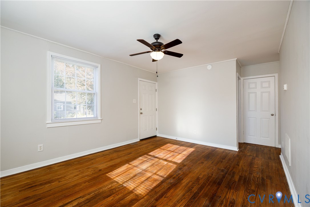 Room featuring wood-finish flooring, a multi-pane window, a ceiling-mounted light fixture with fan, and two interior doors