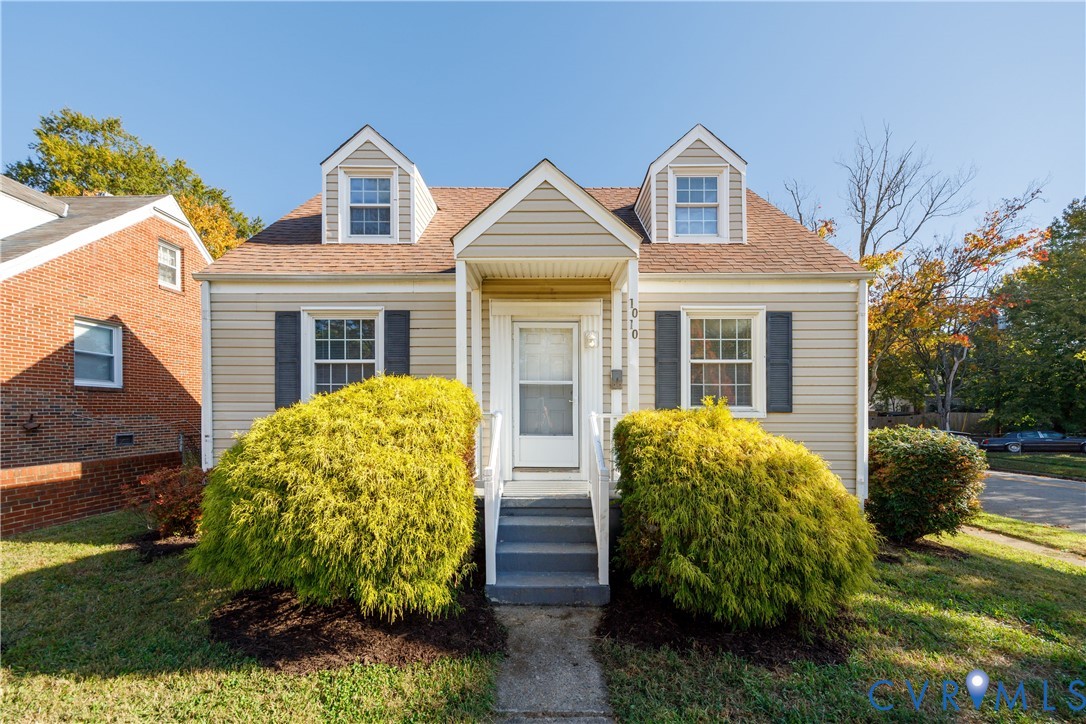 Cape Cod exterior featuring horizontal siding, dual dormer windows, a central gable entrance, and decorative window shutters Cape Cod exterior featuring horizontal siding, dual dormer windows, a central gable entrance, and decorative window shutters