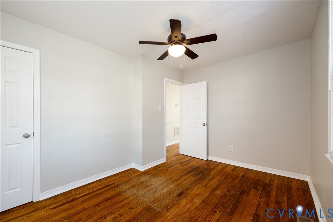 Room featuring wood-finish flooring, six-panel interior doors, and a ceiling-mounted light fixture with a fan