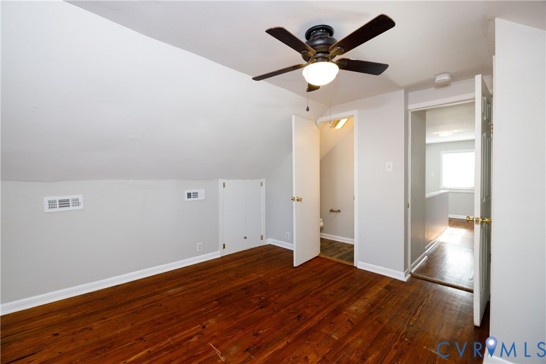 Room featuring wood-finish flooring, sloped ceilings, a ceiling fan with integrated lighting, and built-in under-eave storage