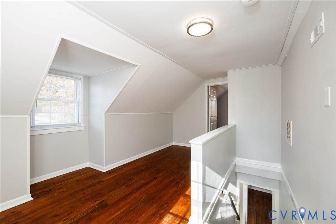 Interior space featuring wood-finish flooring, a vaulted ceiling, a multi-pane dormer window, and a wall-mounted ceiling light fixture