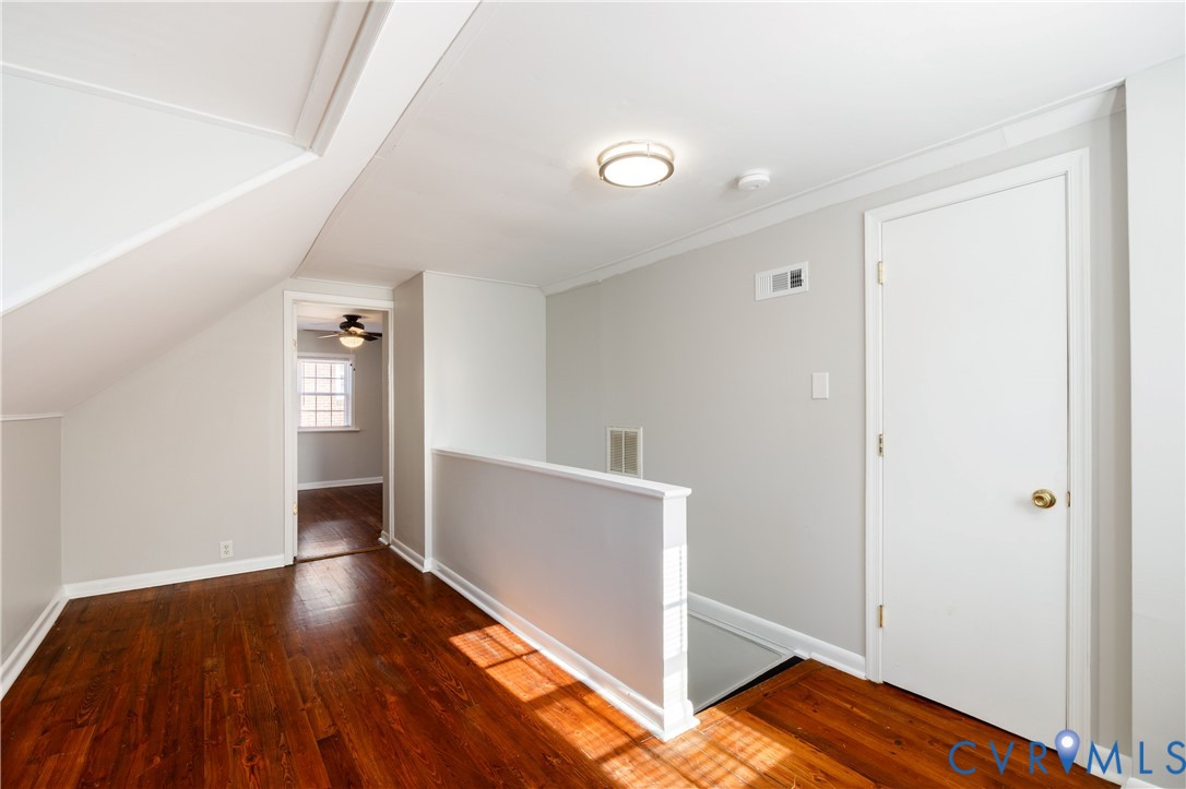 Wood-finish flooring, neutral wall tones, sloped ceiling architecture, and flush-mount ceiling lighting