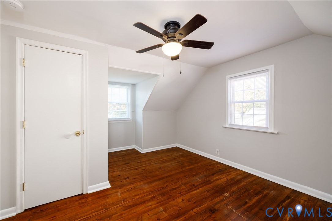 Interior room featuring dark wood-finish flooring, two multi-pane windows, a recessed dormer nook, and a ceiling fan with integrated lighting
