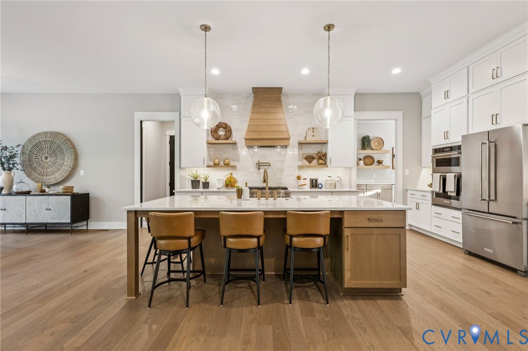 Spacious kitchen featuring a large central island with seating, pendant lighting, wood-finish flooring, white cabinetry, and stainless steel appliances