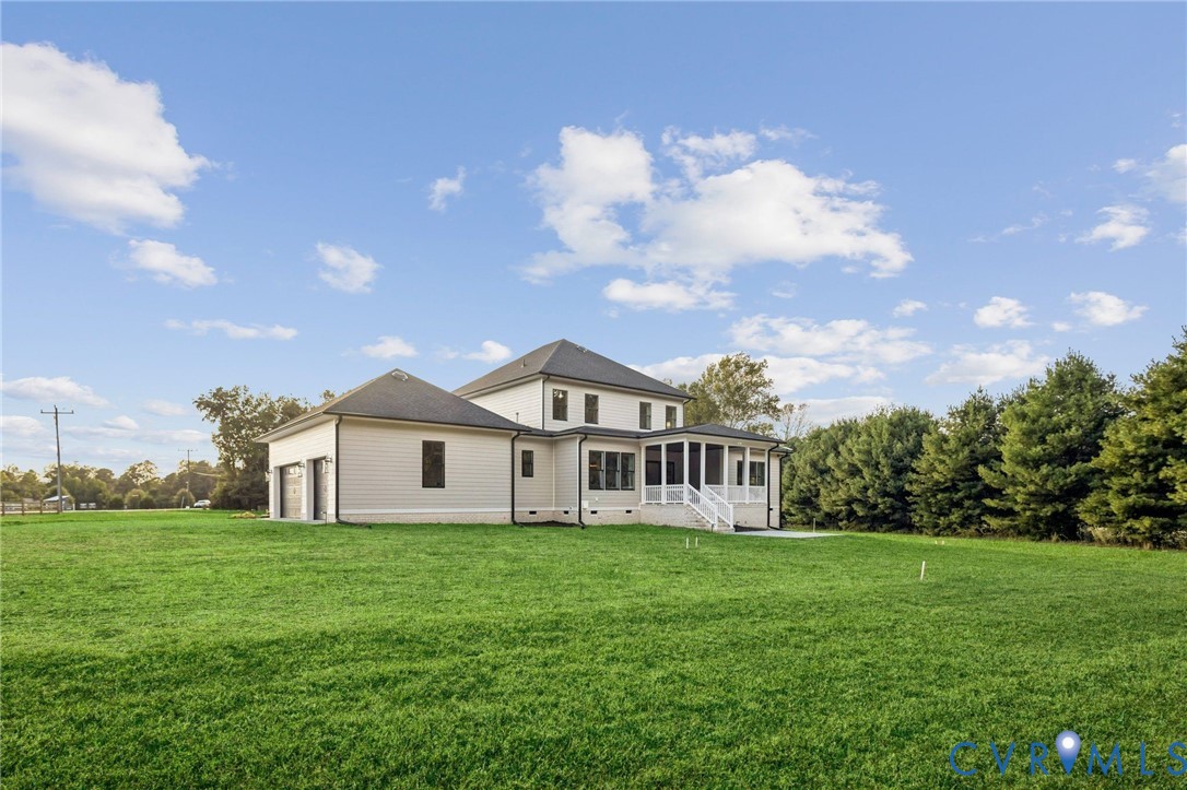 Expansive green lawn surrounds a modern residence featuring a screened-in porch, attached garage, and mature tree line