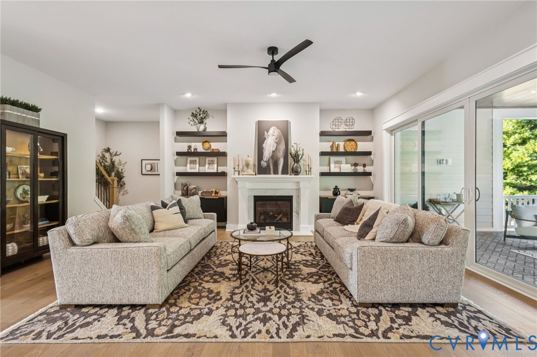 Living area featuring a fireplace with a white mantel, built-in shelving, wood-finish flooring, recessed lighting, and sliding glass doors opening to an outdoor patio