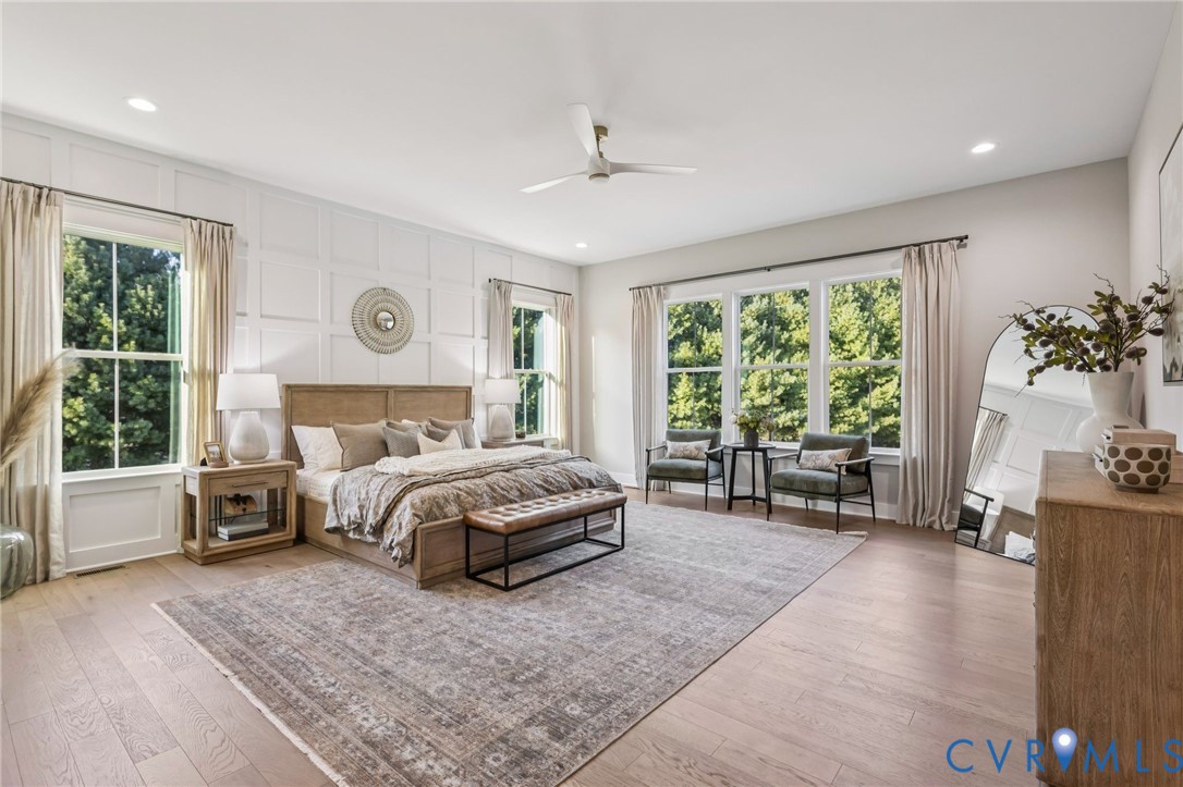 Spacious bedroom featuring light wood-finish flooring, a decorative accent wall, recessed lighting, and a contemporary ceiling fan