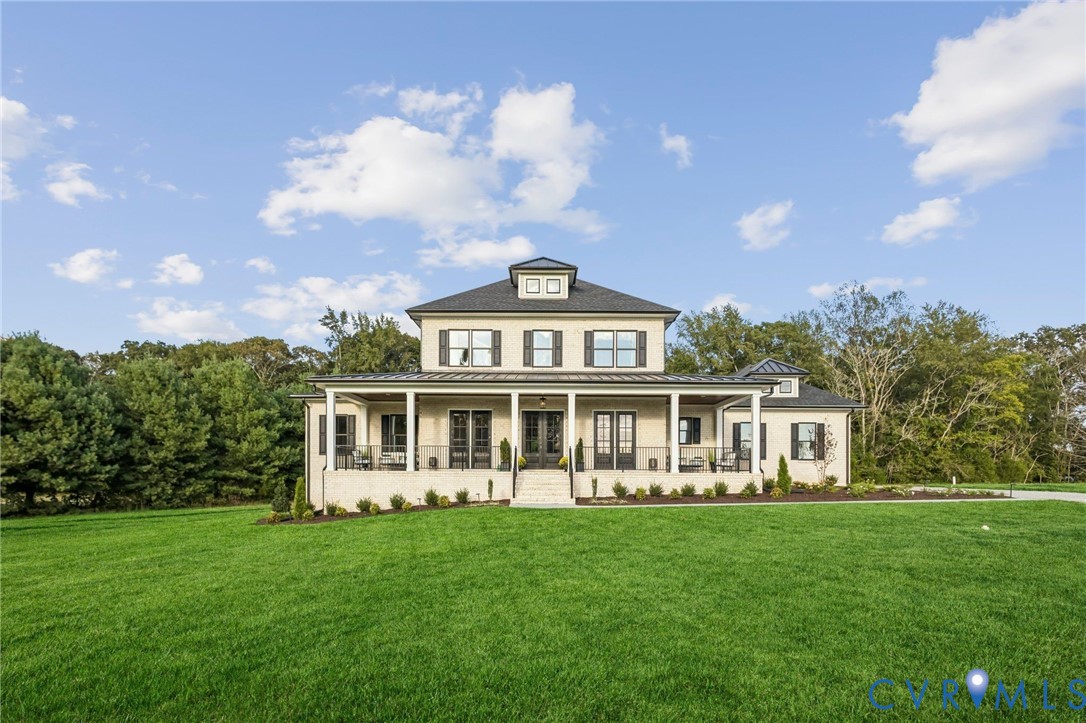 Two-story residence featuring a covered front porch, light-colored brick exterior, dark shutters, and a dark shingle roof Two-story residence featuring a covered front porch, light-colored brick exterior, dark shutters, and a dark shingle roof
