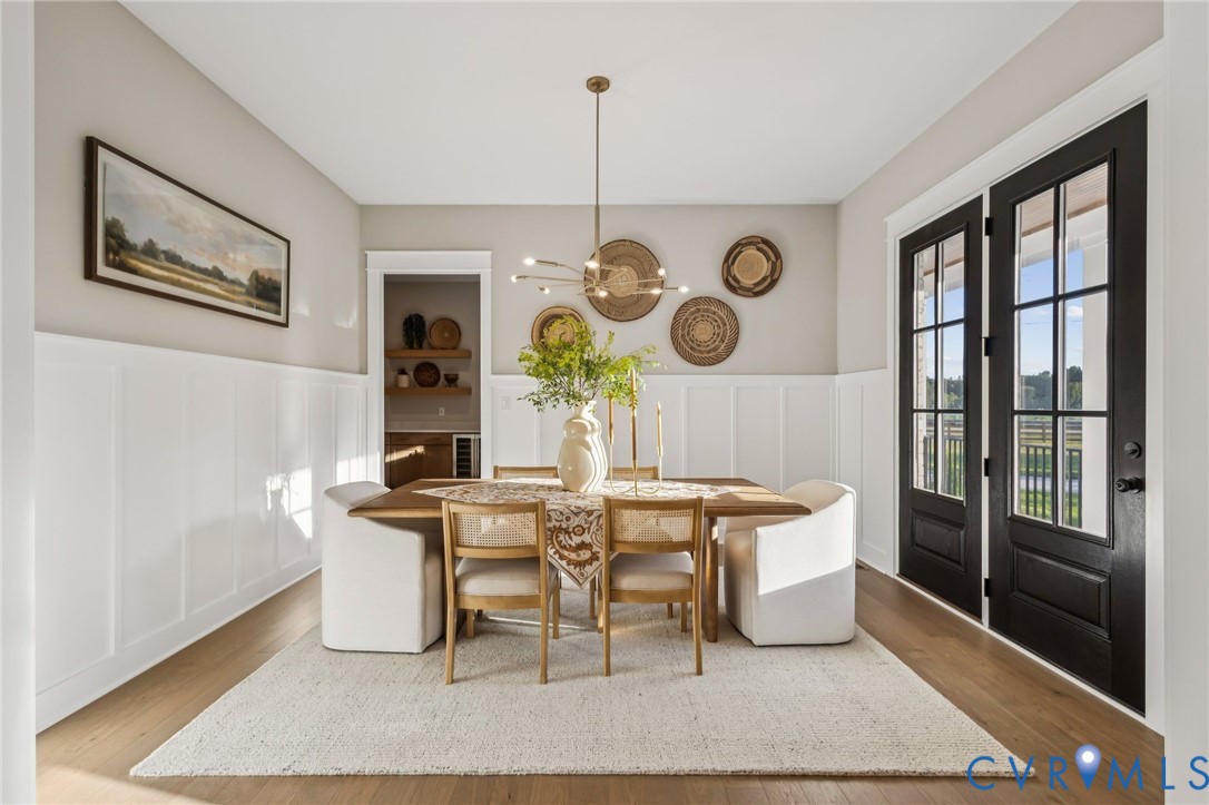 Dining area featuring wood-finish flooring, white wainscoting, and a contemporary linear chandelier
