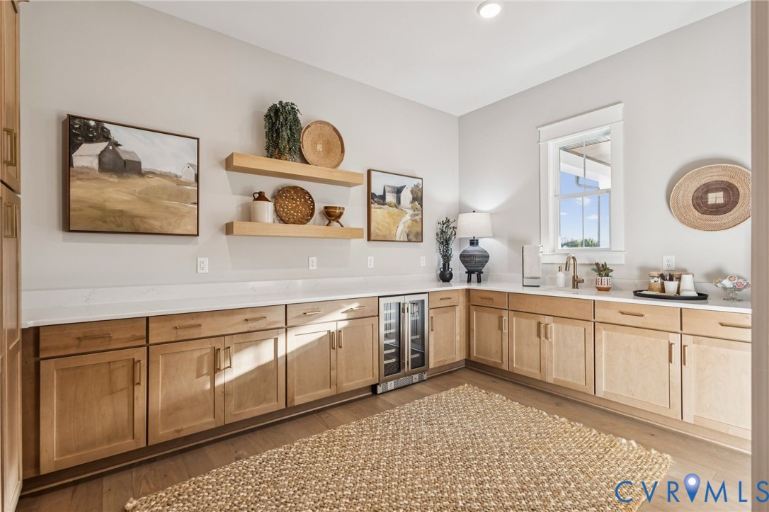 L-shaped built-in cabinetry with light wood-finish doors and drawers, featuring white countertops, a stainless steel beverage refrigerator, and an undermount sink with a gooseneck faucet