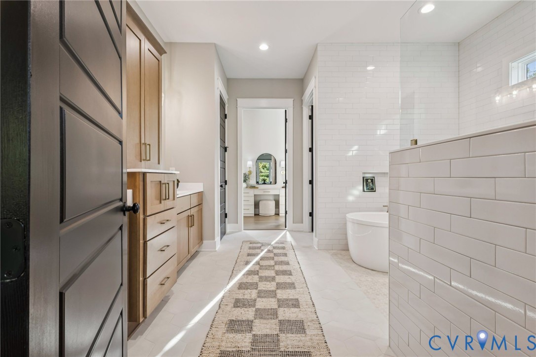 Modern bathroom featuring a freestanding soaking tub, an expansive tiled shower with a glass enclosure, light wood cabinetry with a white countertop, and recessed lighting