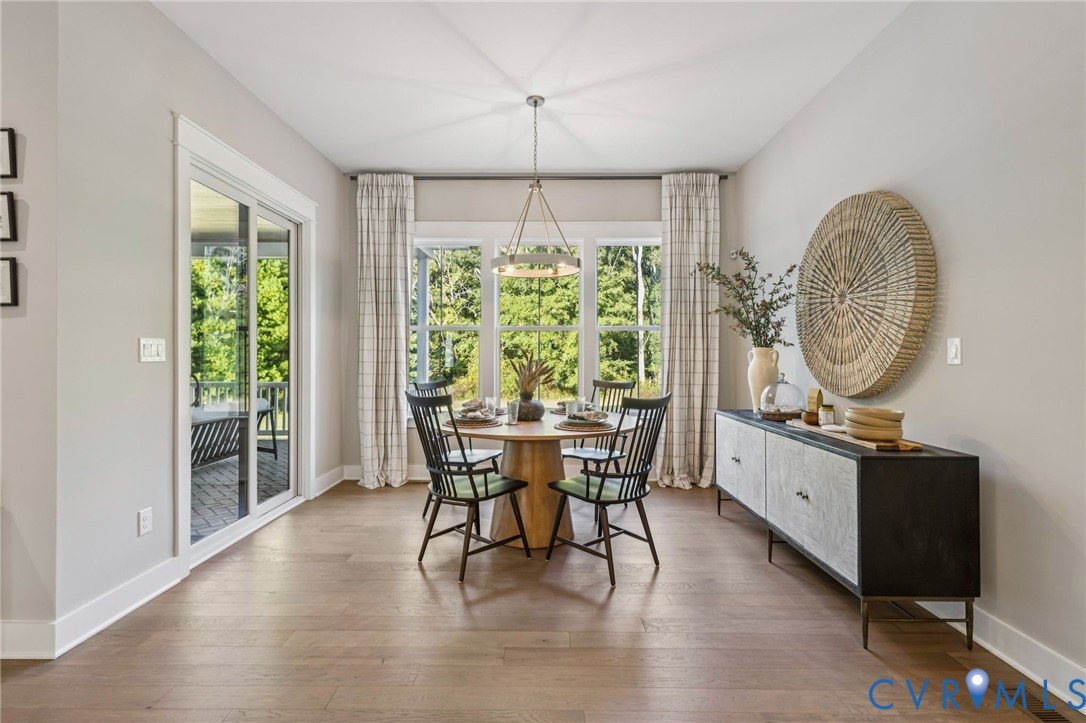 Open-concept dining area featuring wood-finish flooring, a contemporary chandelier, and ample natural light from three large windows