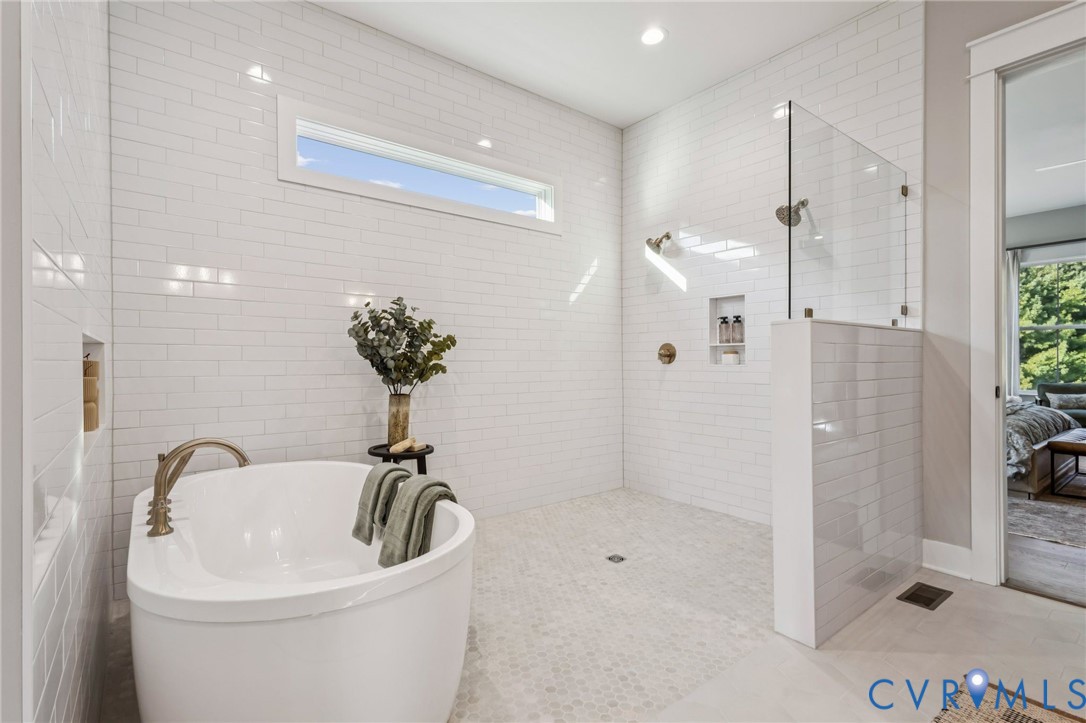 Freestanding soaking tub with a floor-mounted faucet, complemented by a walk-in shower featuring a glass panel, dual shower heads, and built-in niches