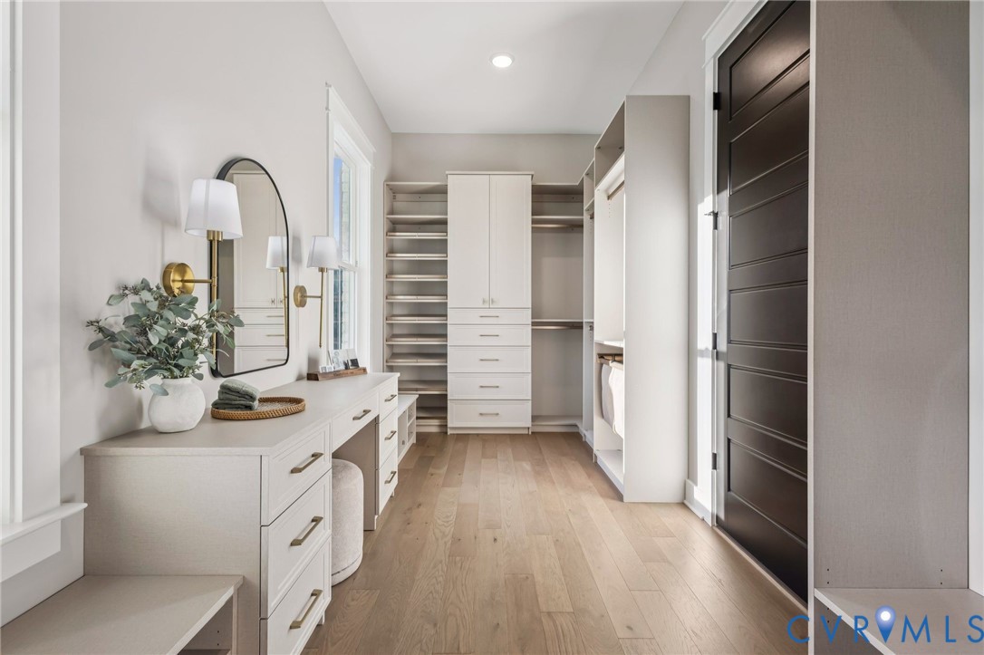 Spacious walk-in closet featuring extensive built-in custom cabinetry, integrated shelving, and light wood-finish flooring