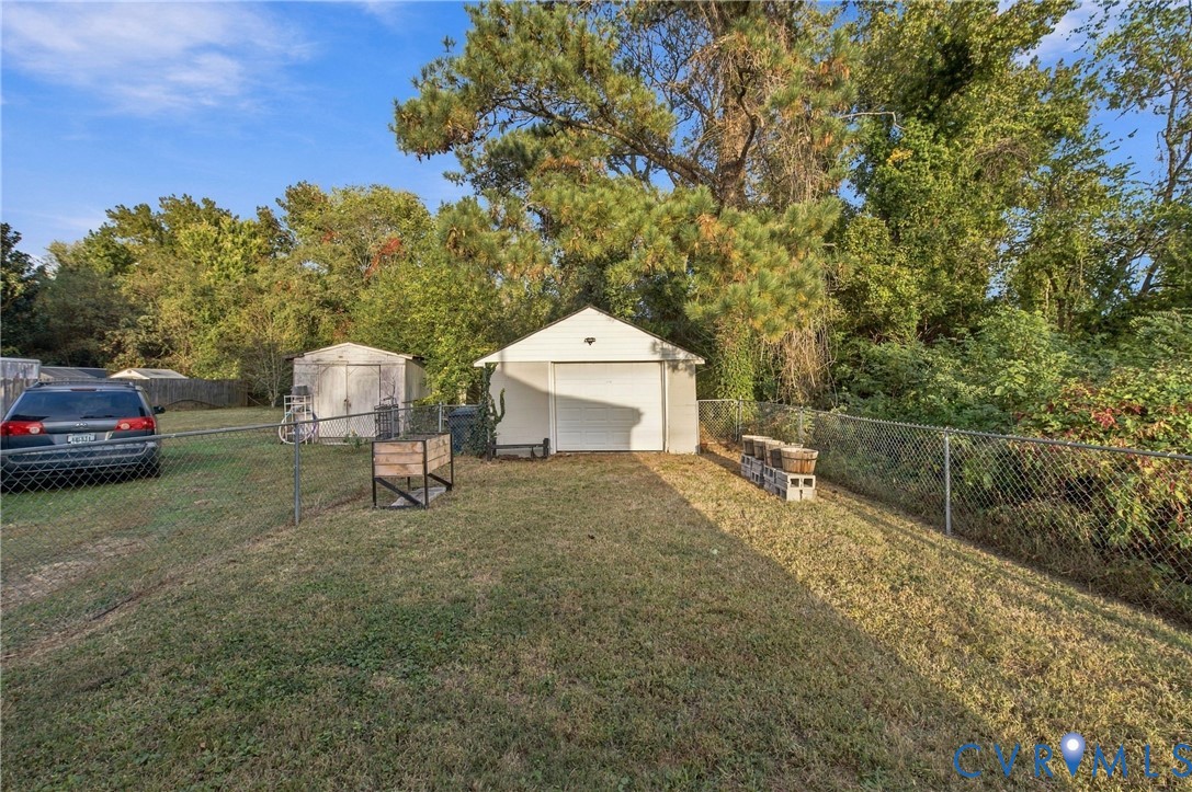 Detached single-car garage featuring a white door, accompanied by a secondary storage shed and chain-link fencing within a grass-covered backyard