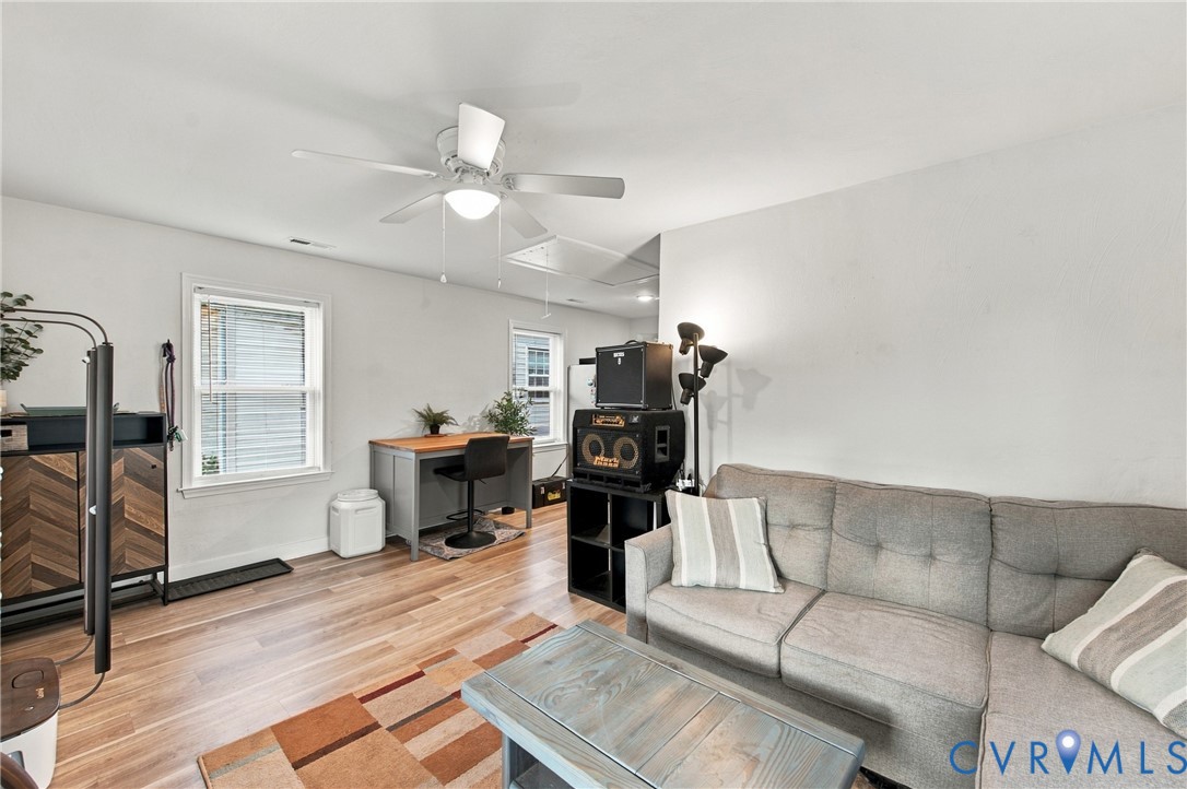 Room featuring wood-finish flooring, dual windows with white casings, and a white ceiling fan with integrated lighting