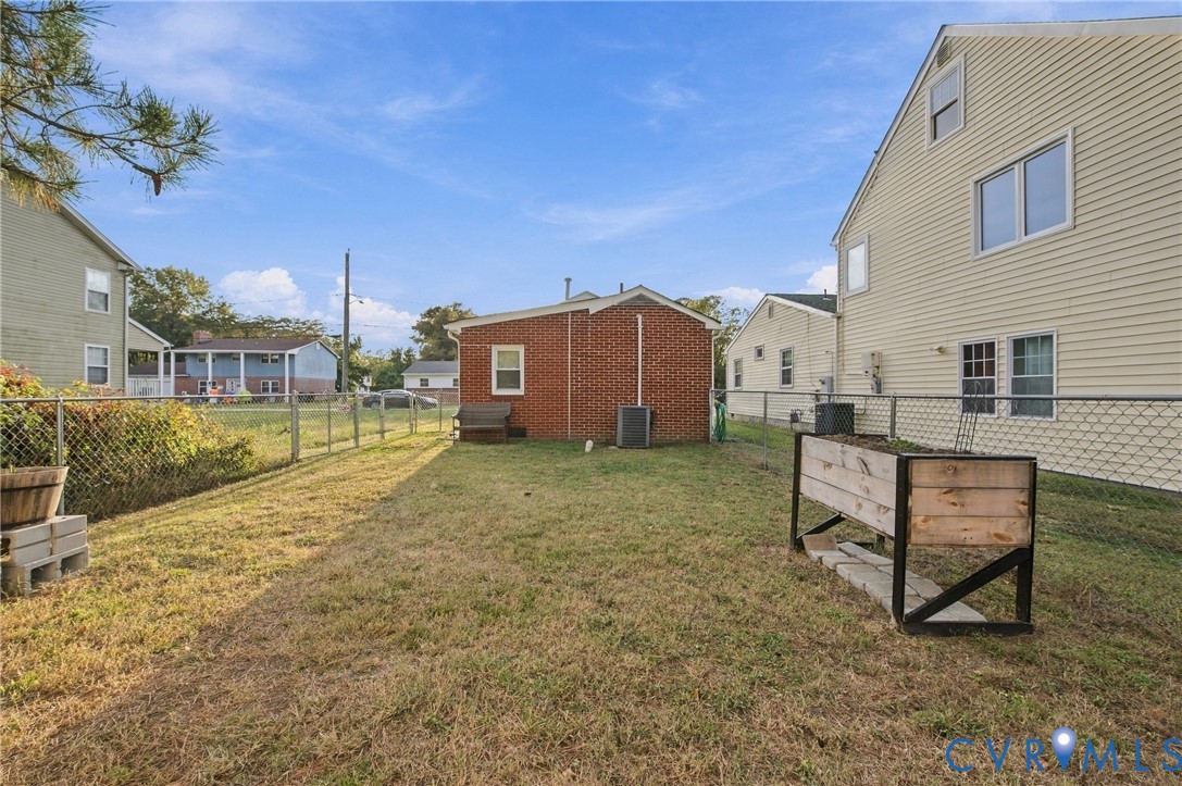 Fenced backyard featuring a brick exterior wall, chain-link perimeter fencing, and grass lawn
