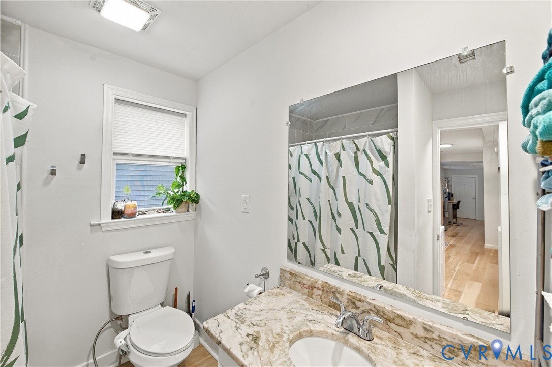 Bathroom featuring a stone-surface vanity with an integrated basin, a large wall-mounted mirror, a tub-shower combination, and a window with horizontal blinds