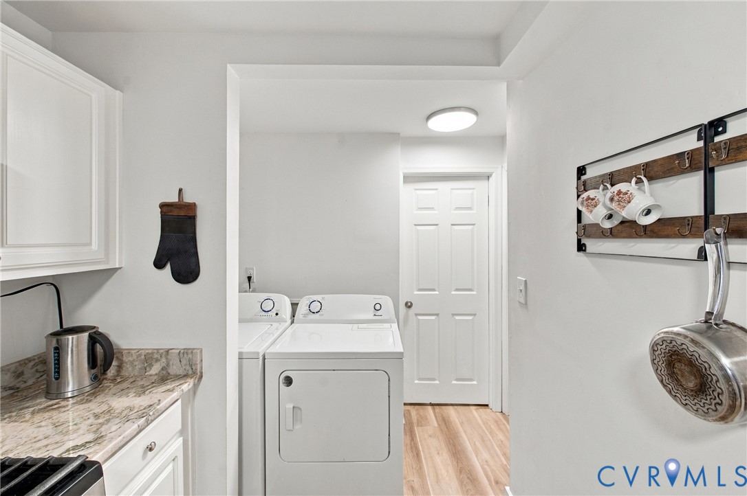 Laundry area featuring stone-look countertop, white shaker-style cabinetry, wood-finish flooring, and a six-panel door