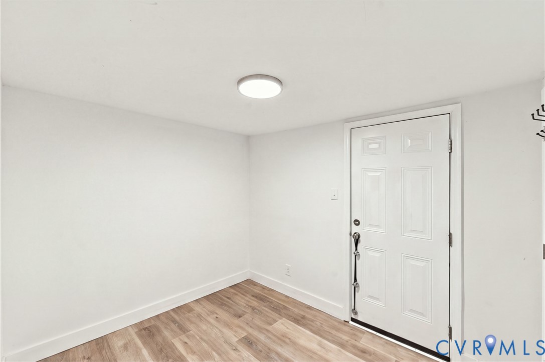 Room featuring neutral walls, wood-finish flooring, and a six-panel door with metallic hardware, illuminated by a flush-mount circular ceiling light