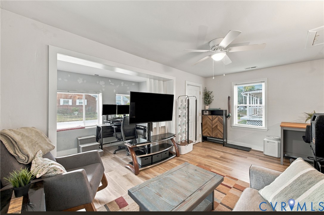 Interior space featuring wood-finish flooring, a ceiling fan with integrated lighting, and multiple windows providing natural illumination