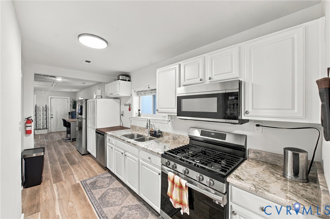 Kitchen featuring white cabinetry, stone-patterned countertops, stainless steel gas range, stainless steel microwave, and wood-finish flooring