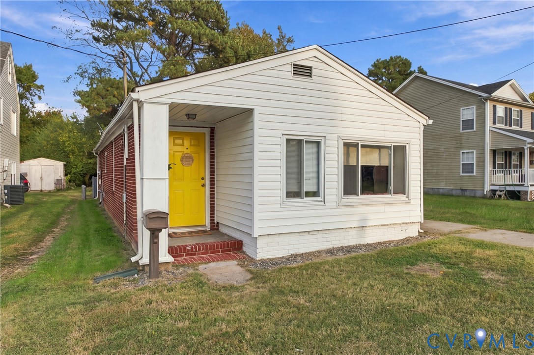 Exterior featuring white horizontal siding, red brick masonry, a covered porch with a brick stoop, and a central entry door