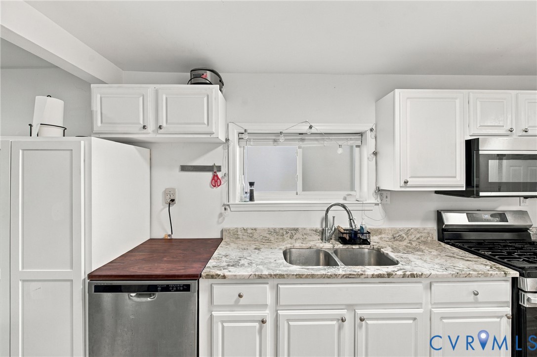 Kitchen featuring white shaker-style cabinetry, stone-patterned countertops, a stainless steel double-basin sink with a gooseneck faucet, and an integrated stainless steel dishwasher