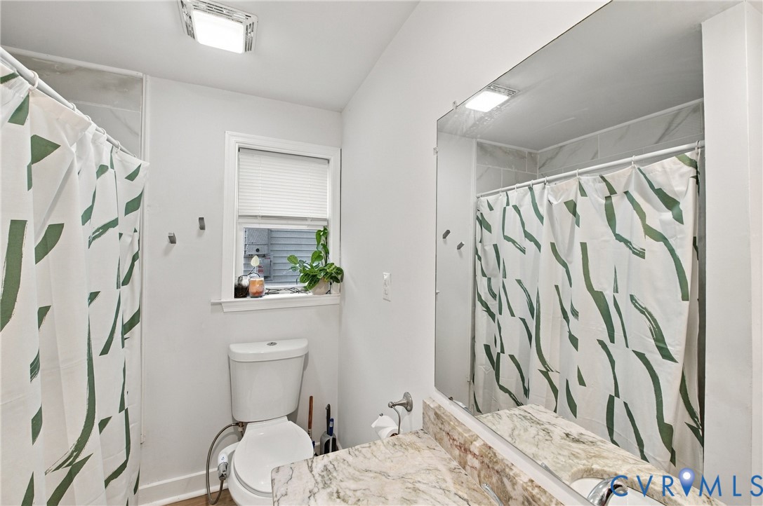 Full-width vanity mirror, stone-finish countertop with an integrated sink, polished chrome faucet, tub-and-shower combination featuring a stone-finish tile surround, and an operable window
