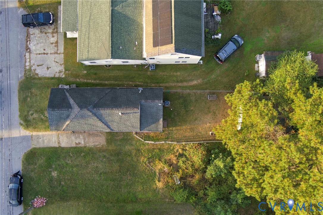 Aerial perspective of a detached structure featuring a multi-pitched roof, shingle exterior, integrated solar panels, and an open-concept lot with mature landscaping