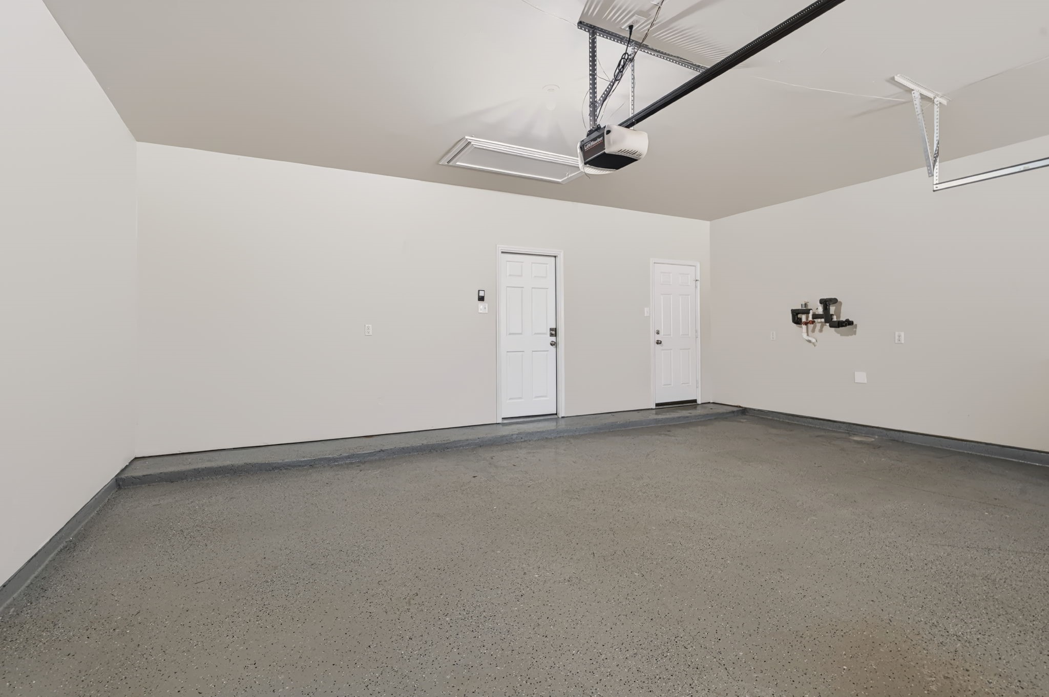 Spacious 2.5-car garage featuring an epoxy-coated floor, a pull-down attic ladder for additional storage, and an existing hookup for a water softener.