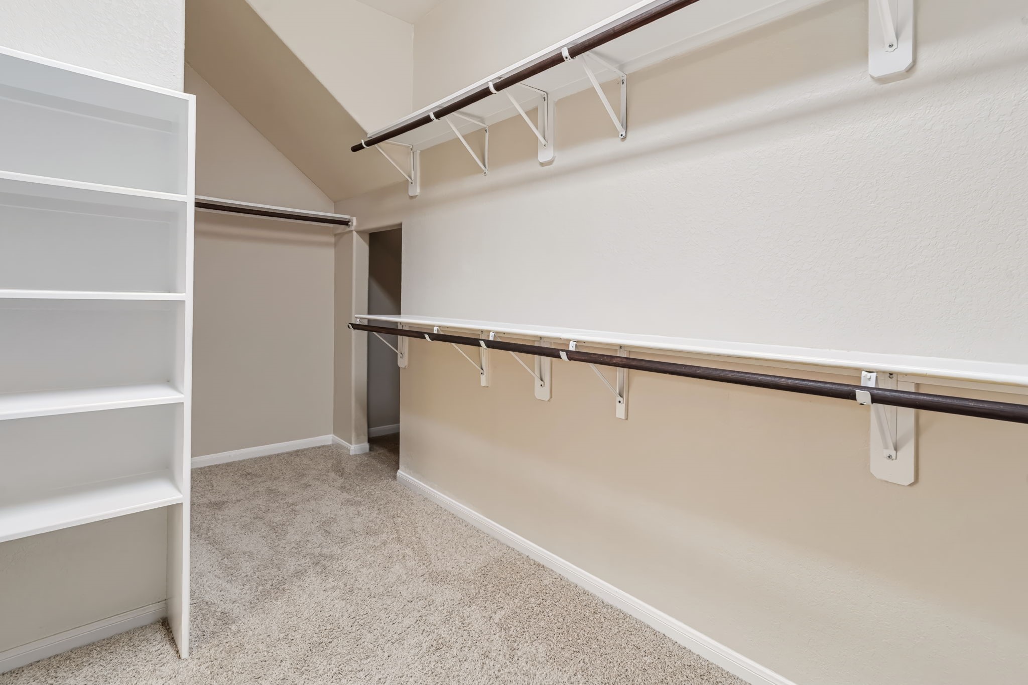 The spacious primary suite walk-in closet features built-in shelving, double hanging racks, and additional under-stair storage, providing ample room for clothing, accessories, and luggage.