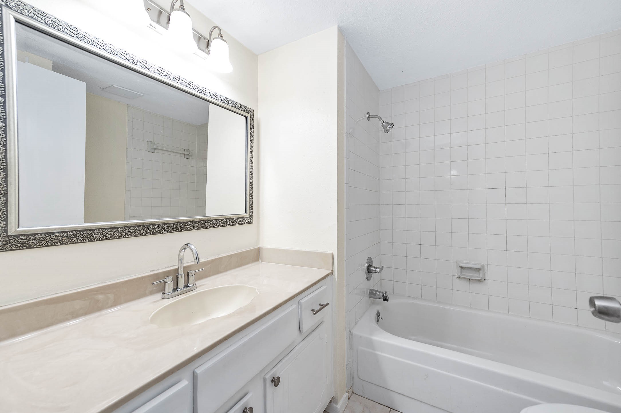 Bathroom features a clean design, large mirror and designer lighting, spacious vanity. Bathtub with tiled walls Combination shower.