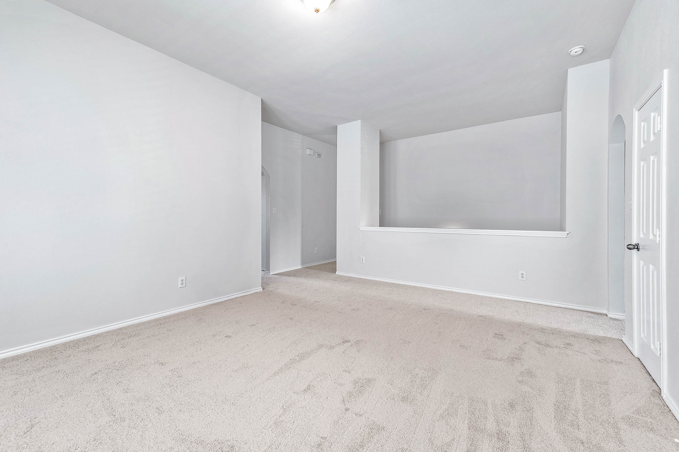 This spacious LOFT features neutral-toned carpet and walls, providing a blank canvas for customization. It includes a partial wall divider and an open doorway, offering potential for versatile use.