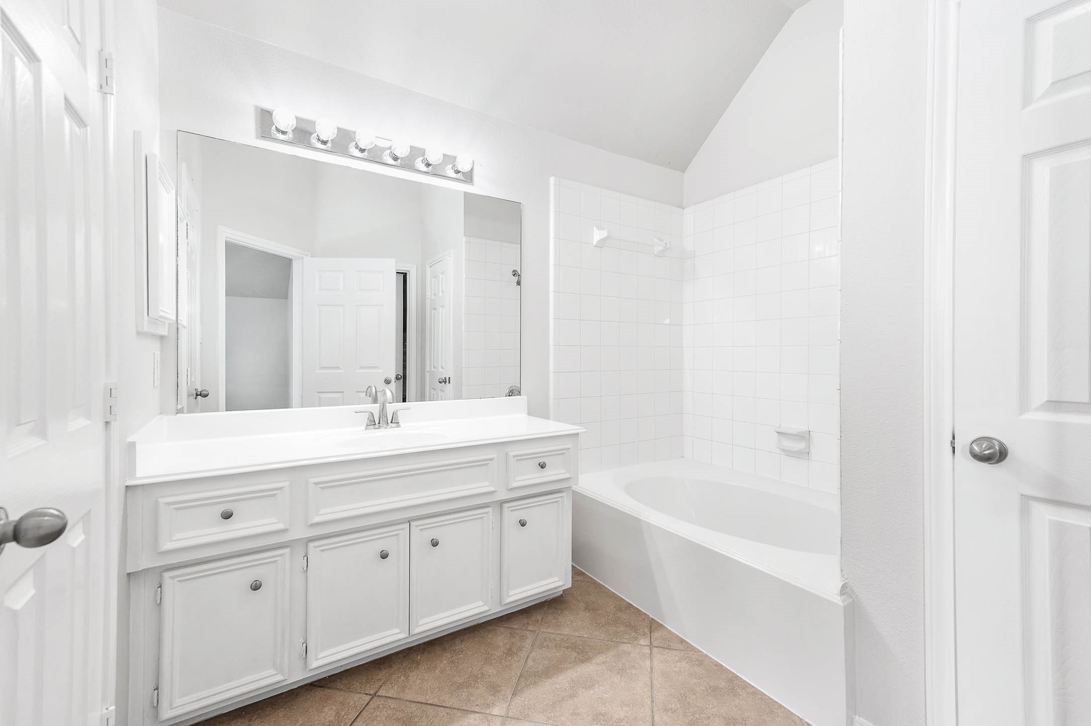 This bathroom features an OVERSIZE GARDEN Bathtub -ENJOY ! Clean design with a large vanity, ample storage, a spacious mirror with modern lighting, and a tiled shower-bathtub combo. The neutral tile floor complements the white cabinetry and walls.