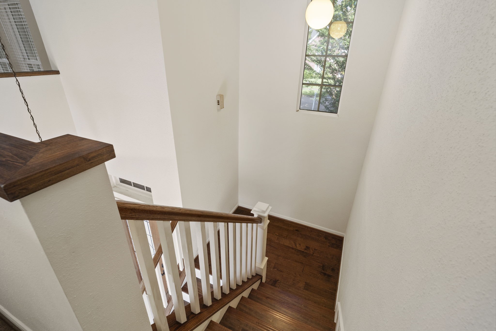 Hardwood stairs & flooring add warmth, while a tall window brings natural light into the stairway.