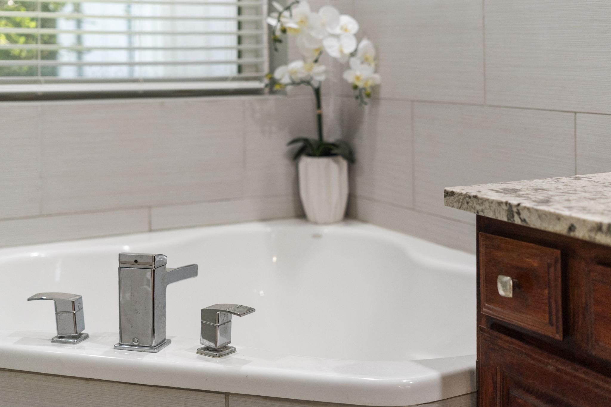 A deep soaking tub surrounded by modern tile creates a relaxing focal point within the updated primary bath.