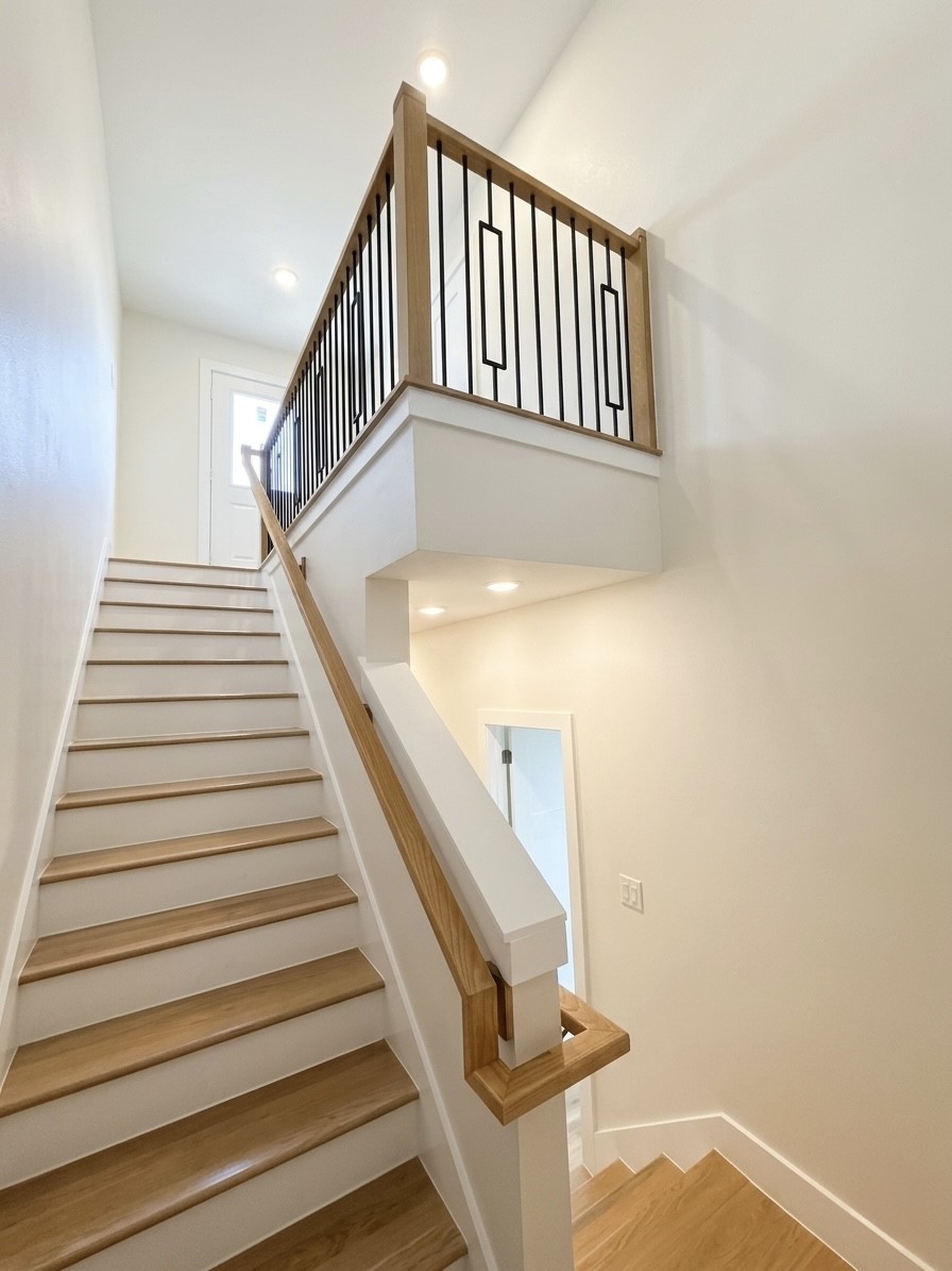 Bright and modern staircase with sleek wood accents and elegant iron railings, leading to an inviting upper level.
