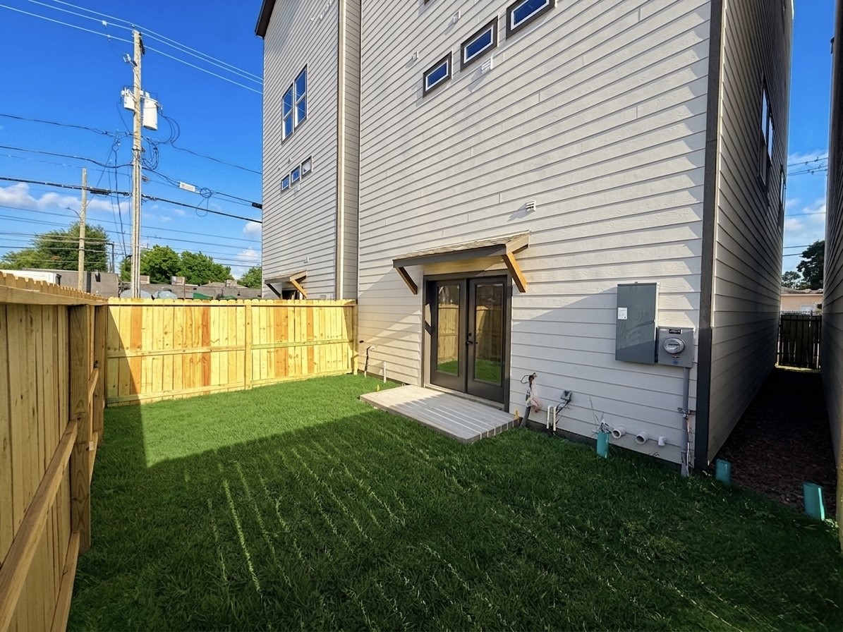 Charming backyard with lush green grass, privacy fencing, and convenient access through elegant double doors, perfect for outdoor relaxation and entertainment.