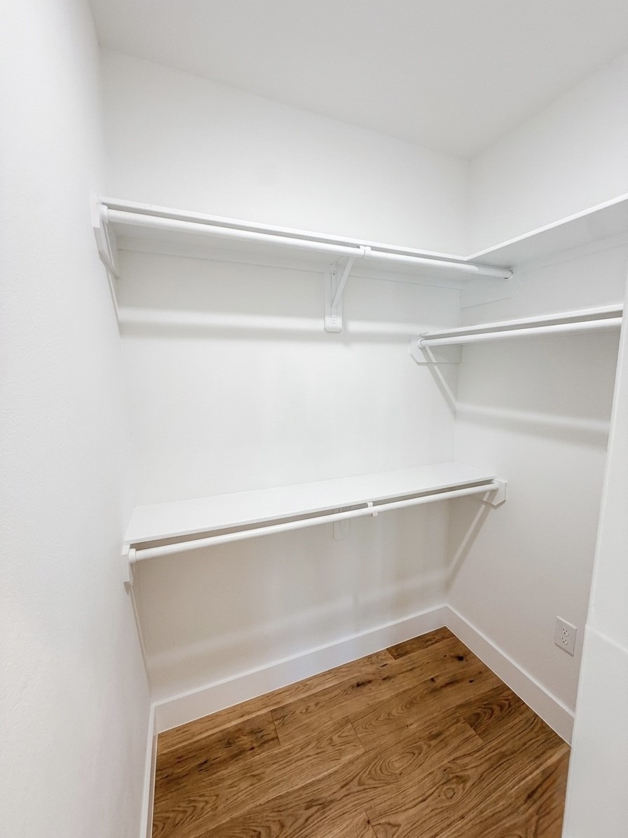 Spacious walk-in closet featuring sleek white shelving and ample hanging space, with elegant porcelain flooring for a modern touch.