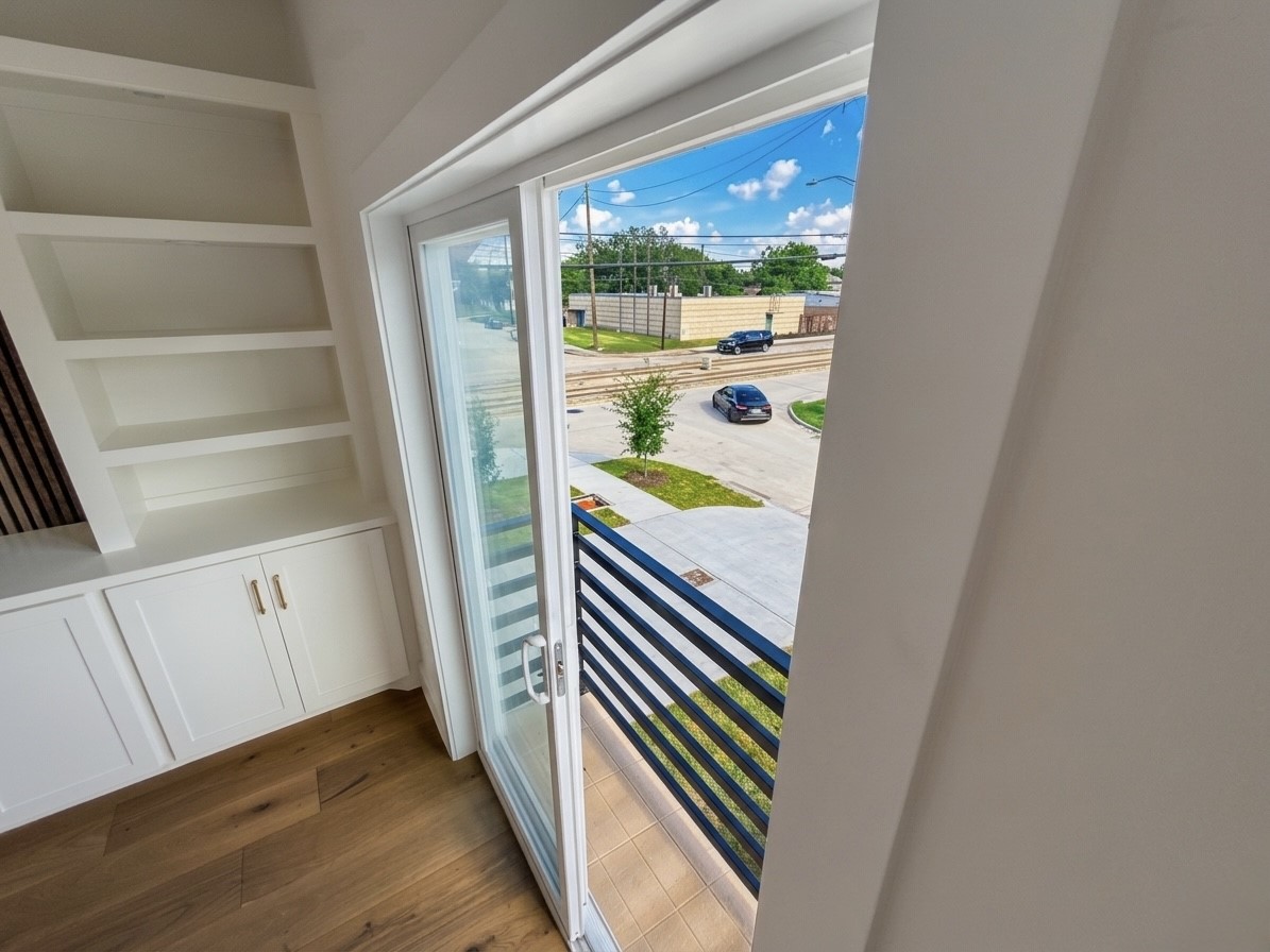 Bright room with built-in shelving and hardwood floors, featuring a sliding glass door leading to a balcony with street views.
