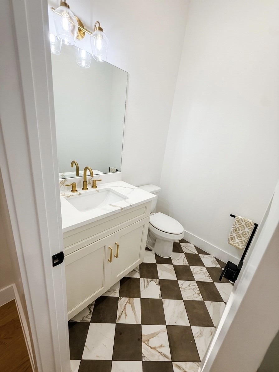 Chic bathroom with a modern vanity featuring gold fixtures, a large mirror, and stylish checkered tile flooring.