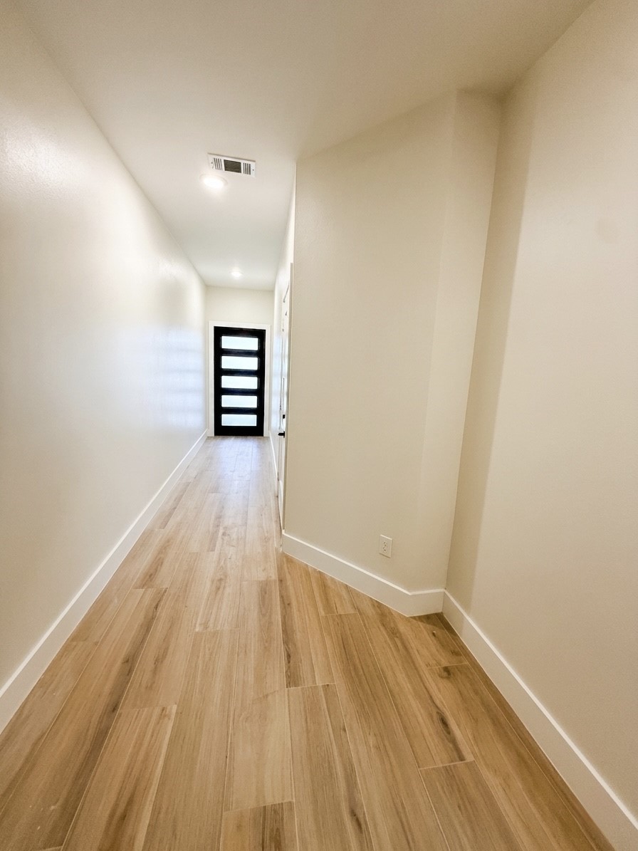 A sleek, modern hallway with light porcelain flooring and a contemporary door at the end, offering a warm and inviting entrance.