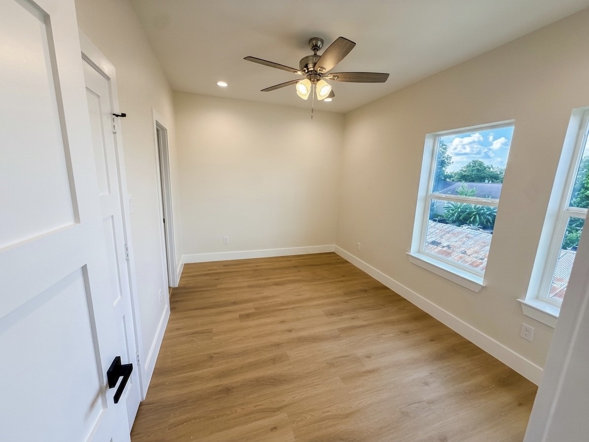 Bright and inviting room featuring sleek hardwood engineered floors, a modern ceiling fan, and large windows offering scenic views.