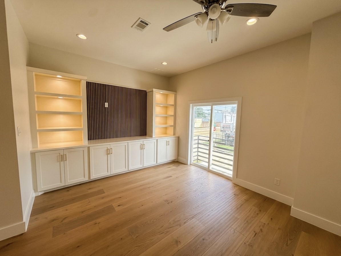 Bright, spacious room featuring built-in illuminated shelving, elegant cabinetry, and a large sliding glass door leading to an outdoor view.