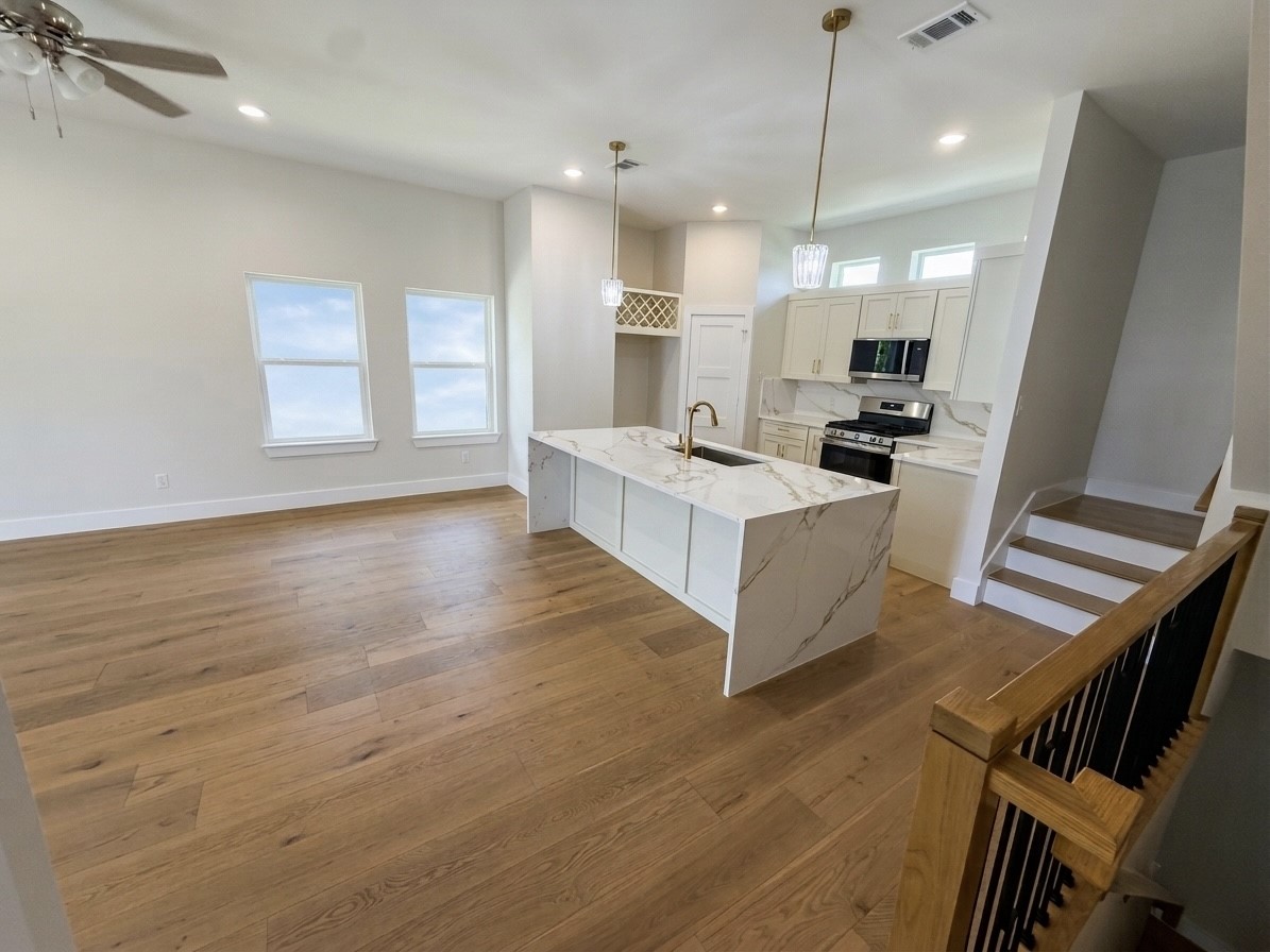Bright and open kitchen with a large quarts island, elegant pendant lighting, and modern stainless steel appliances, seamlessly flowing into a spacious living area with hardwood engineered floors.