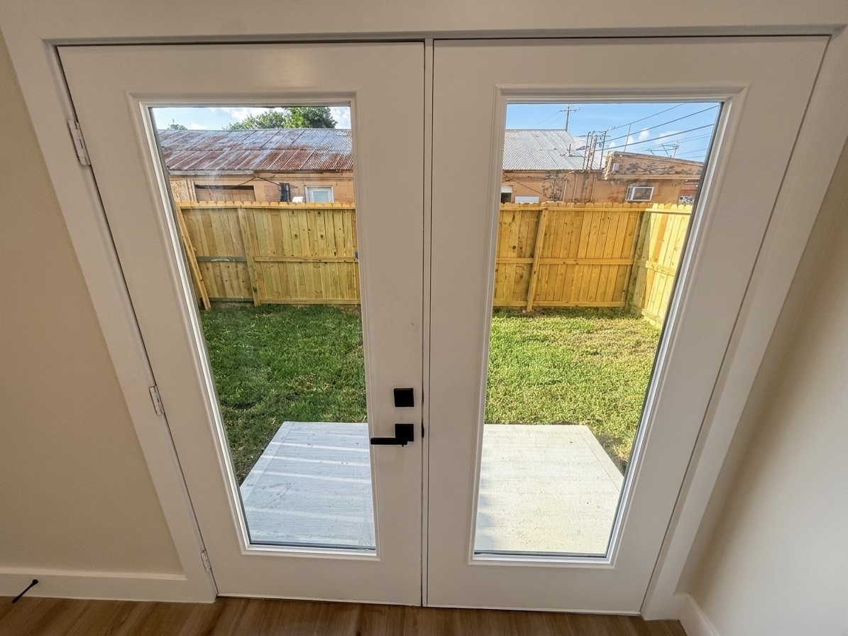 Elegant French doors open to a cozy backyard with a wooden privacy fence, perfect for enjoying outdoor relaxation.