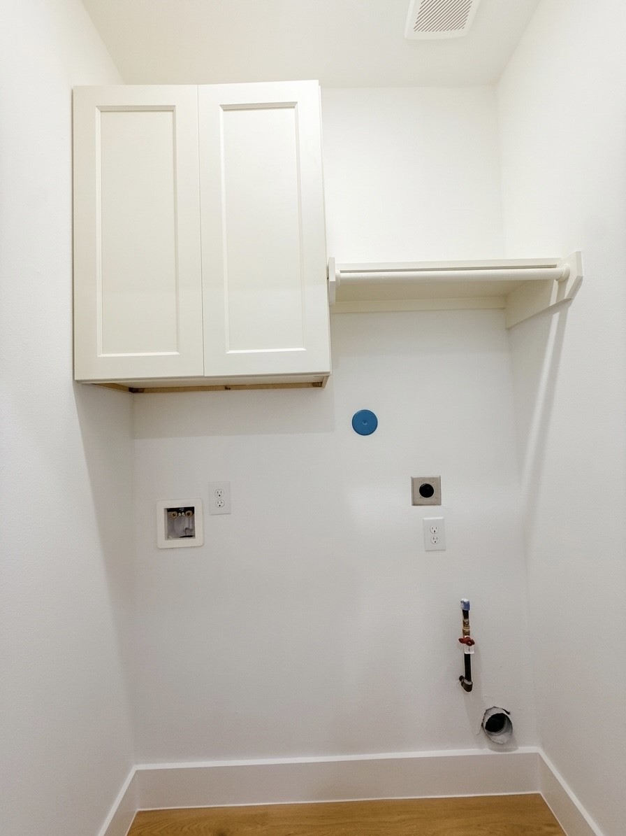 Compact laundry area with hookups, featuring upper cabinetry and a convenient hanging rod for additional storage.
